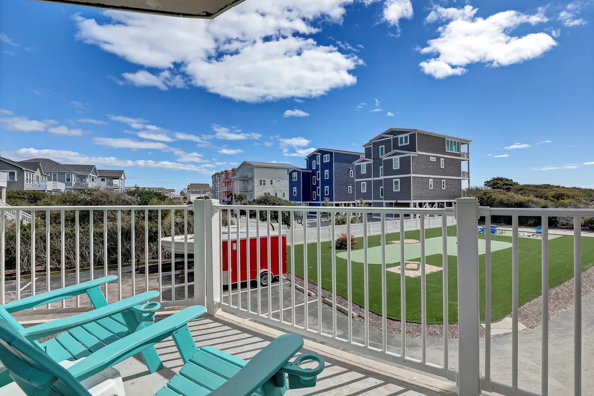 An exterior balcony scene with turquoise chairs, blue sky, and colorful resort buildings. The setup invites guests to relax, socialize, and enjoy sunset views or morning coffee together, with a cheerful resort backdrop.
