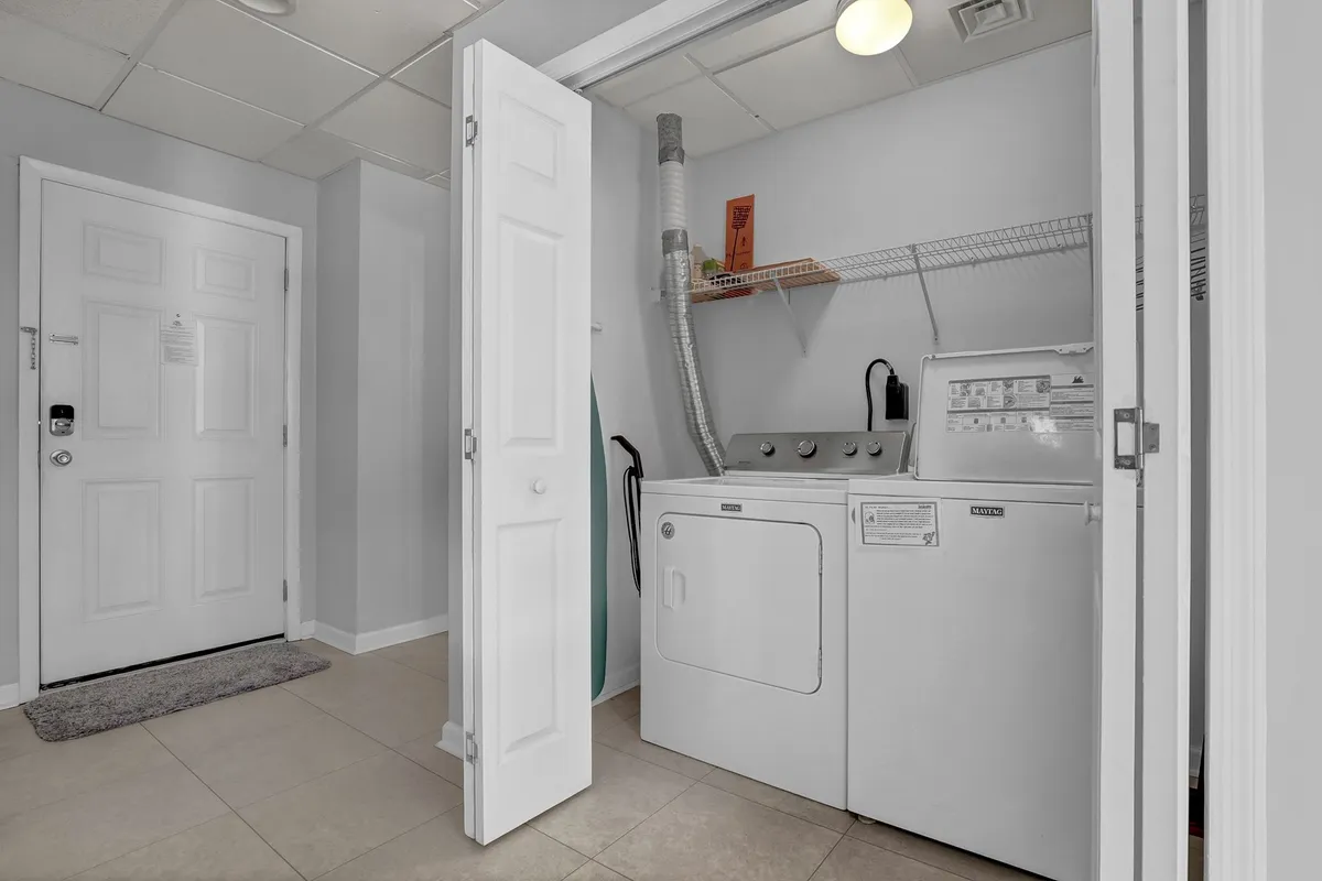 A compact laundry area with a washing machine, dryer, and ironing board neatly arranged for convenience. The practical setup is ready for sandy beach clothes and longer stays.