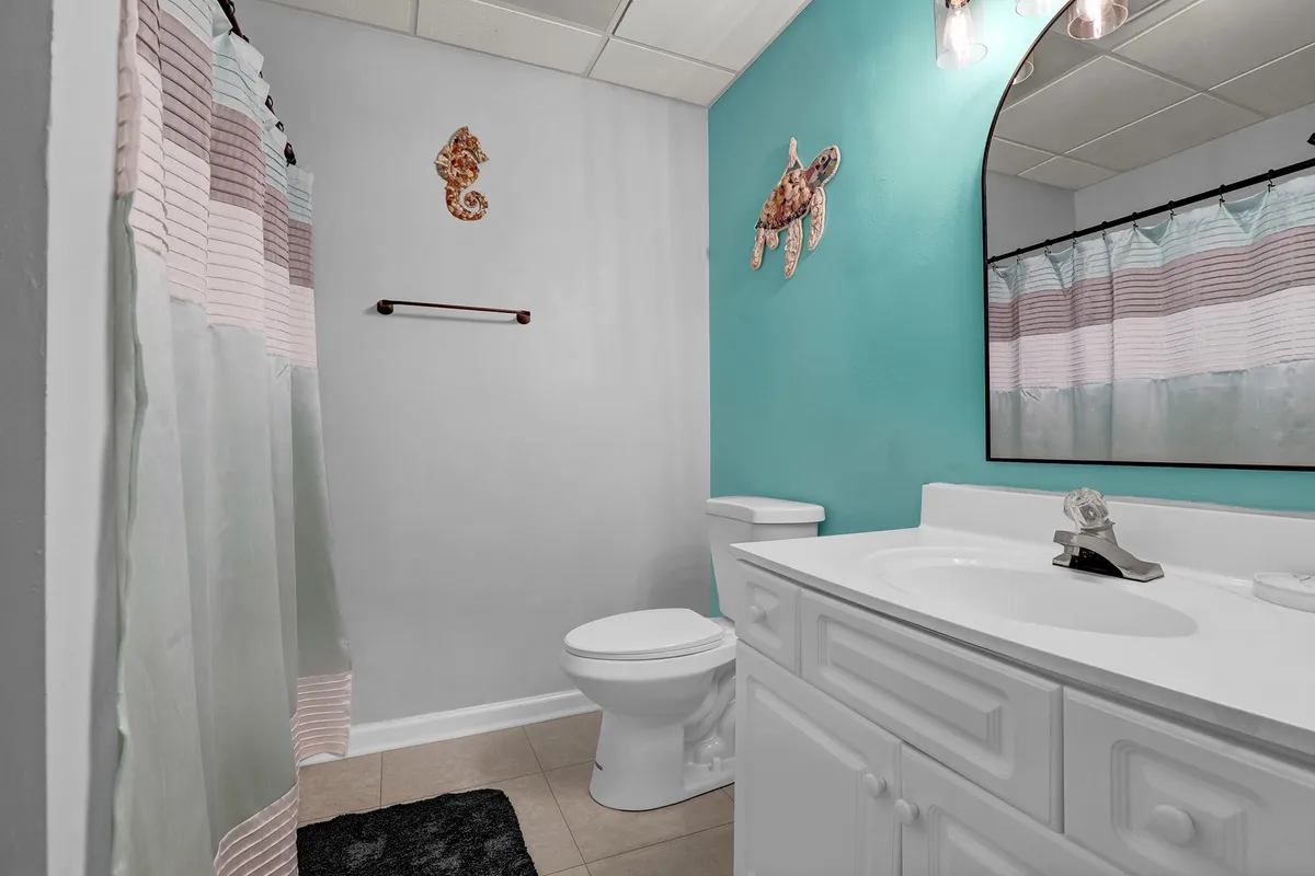 A cheerful bathroom scene with colorful wall art, a vanity mirror, and a shower curtain. The space is bright and inviting, ideal for starting or ending the day with comfort.