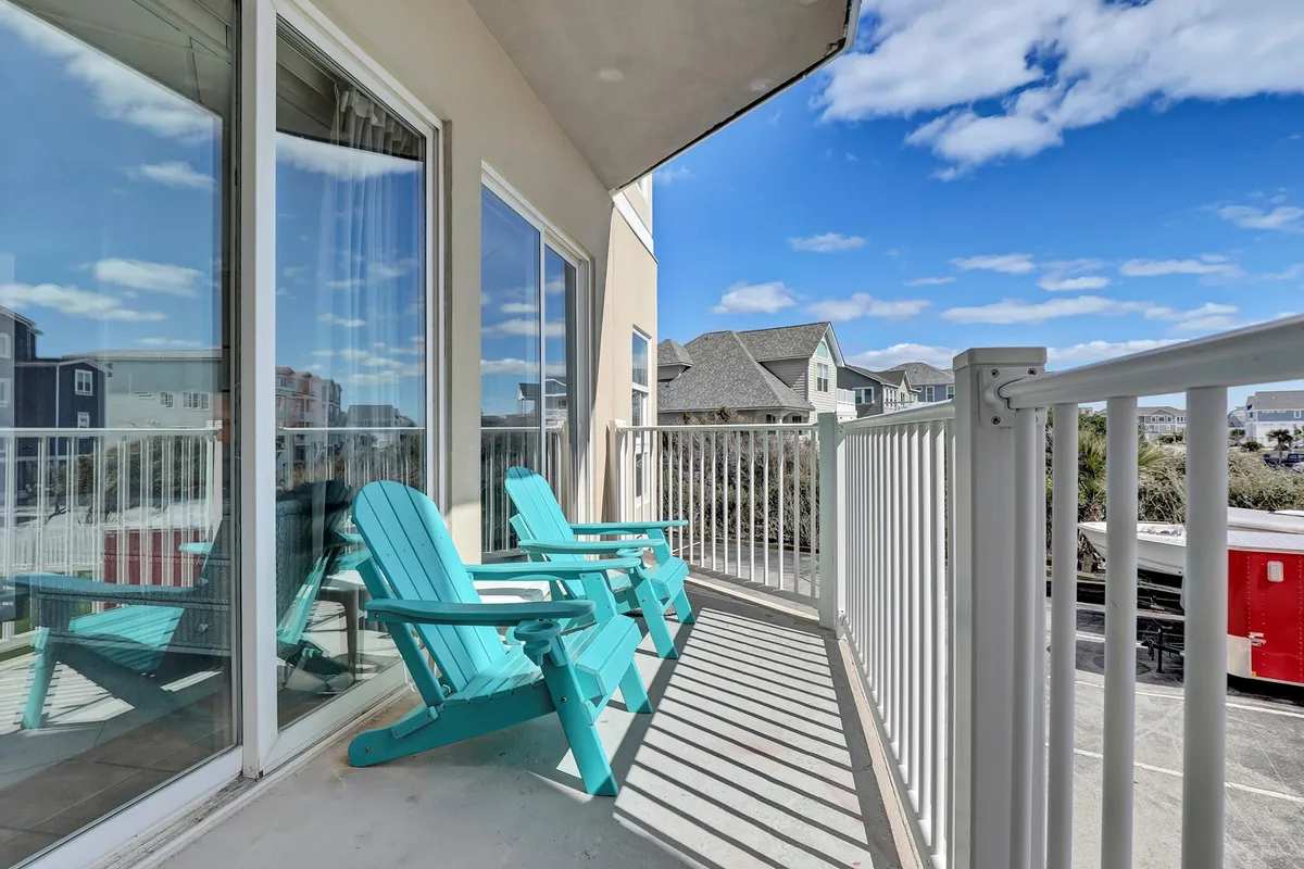 This exterior image features turquoise Adirondack chairs positioned on a balcony or patio with large windows and a clear blue sky in the background. The setting overlooks an inspiring view—likely of the ocean—inviting peaceful moments and relaxation, perfectly capturing the tranquil coastal atmosphere.