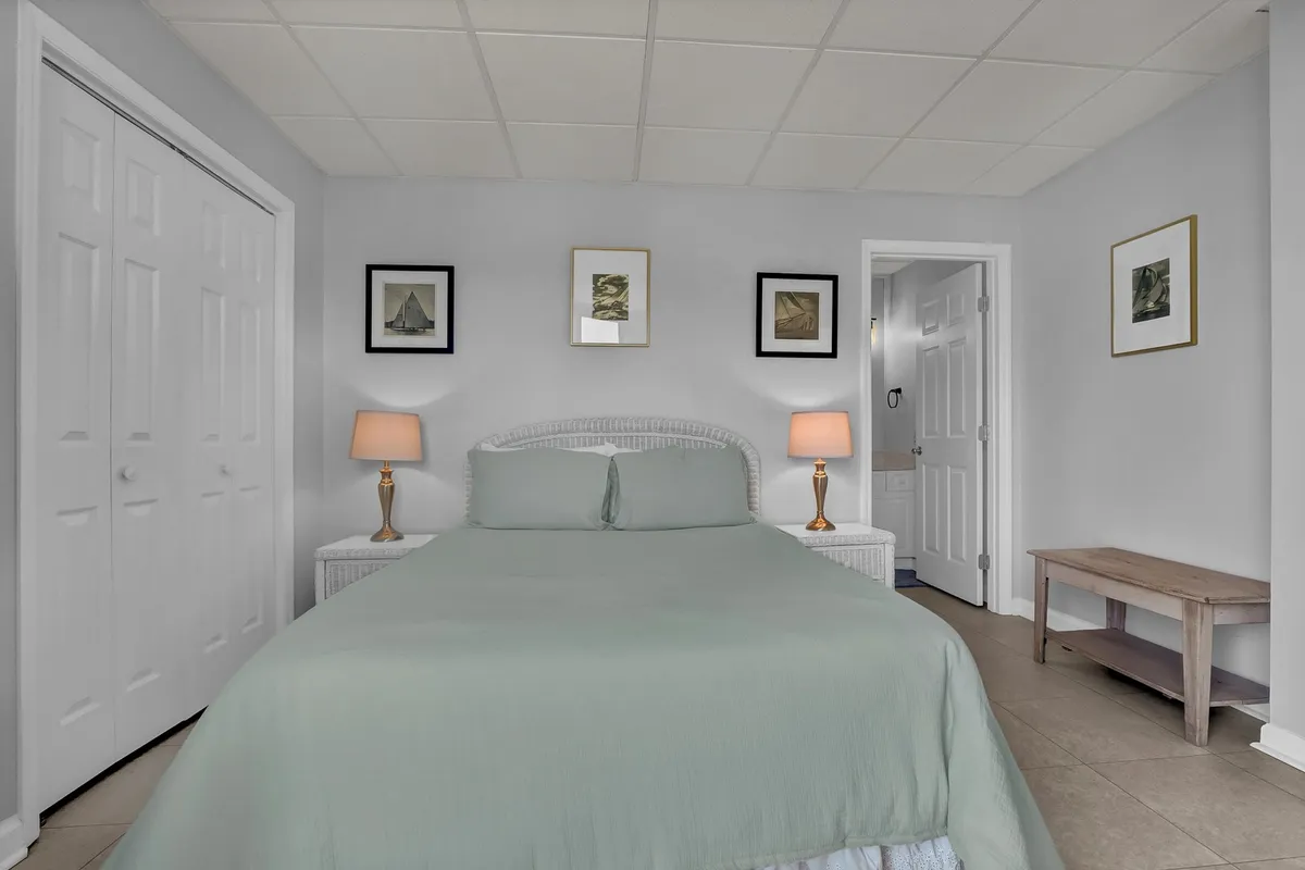 A tranquil bedroom with light green bedding, warm table lamps, framed artwork, and closet doors. The room emanates a sense of peace and flexibility, perfect for restful nights and personal touches.