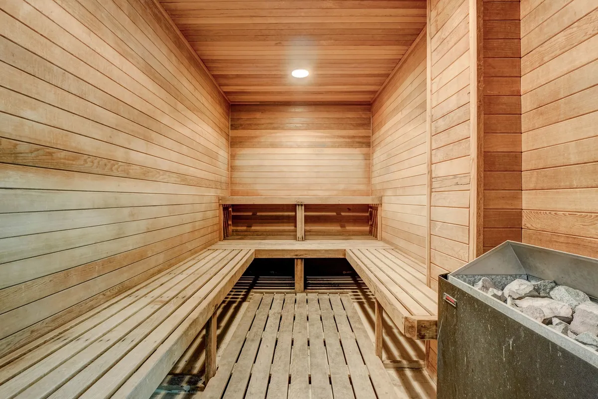 A calming sauna room with wooden benches, wooden walls, and a sauna heater, suggesting a space for relaxation and rejuvenation. The warm tones create a spa-like atmosphere.